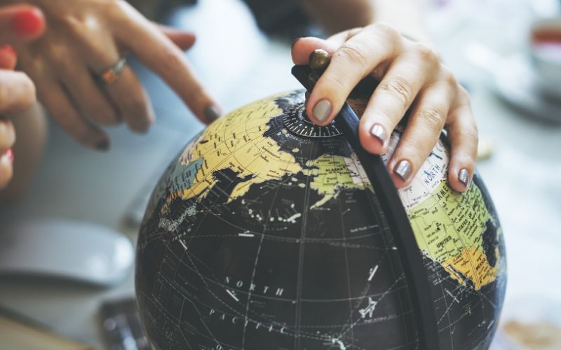 a woman's handing golding a desk top globe and pointing to a continent