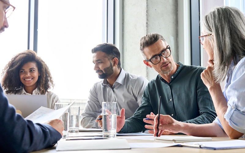 diverse group of people discussing and smiling at a table in a workplace