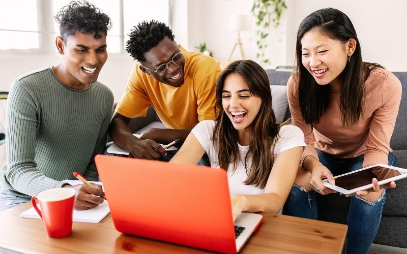 Millennials sitting around a laptop smiling and laughing