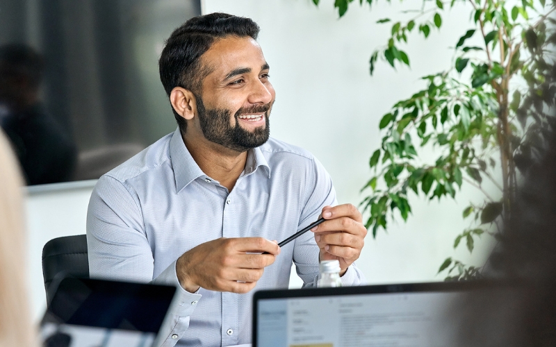 Business man behind computer smiling and holding a pen