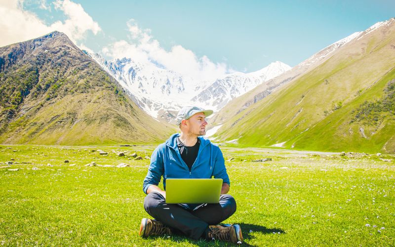 Man looking to the side with a laptop in the mountains